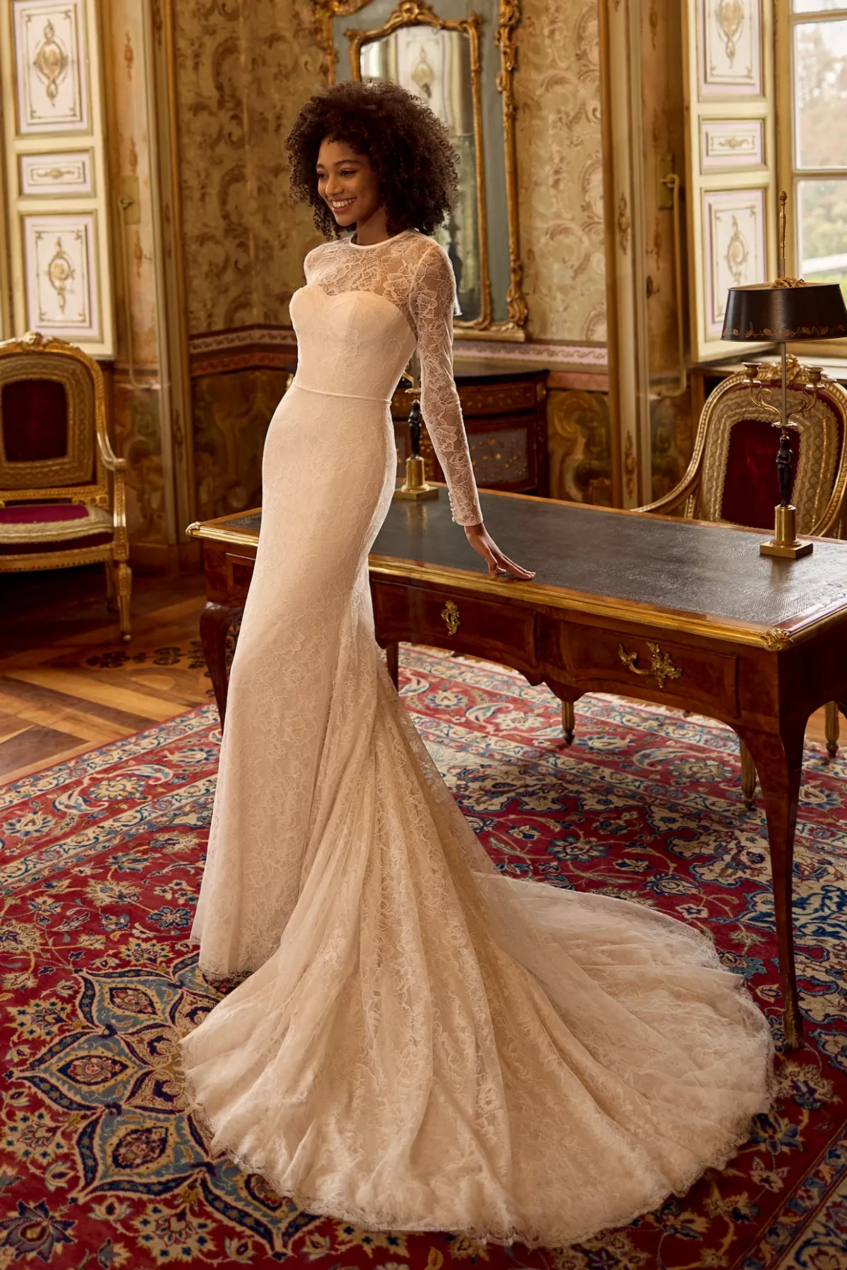 A model showcases the Ines Di Santo Entasis dress from the Ines by Ines Di Santo collection near a writing desk in a mansion