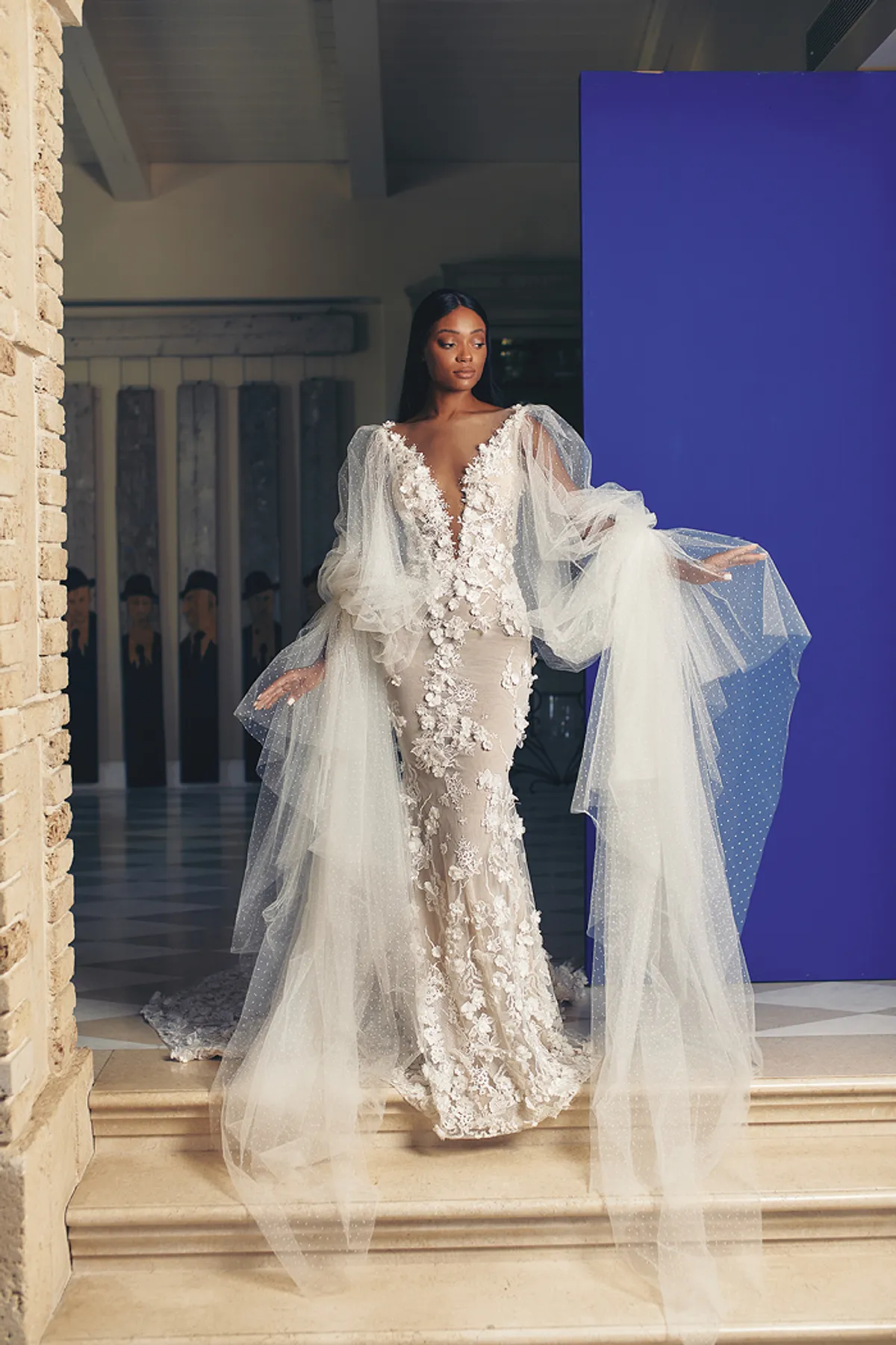 A model showcases the Galia Lahav Fleur dress from the Couture collection on a staircase inside a house