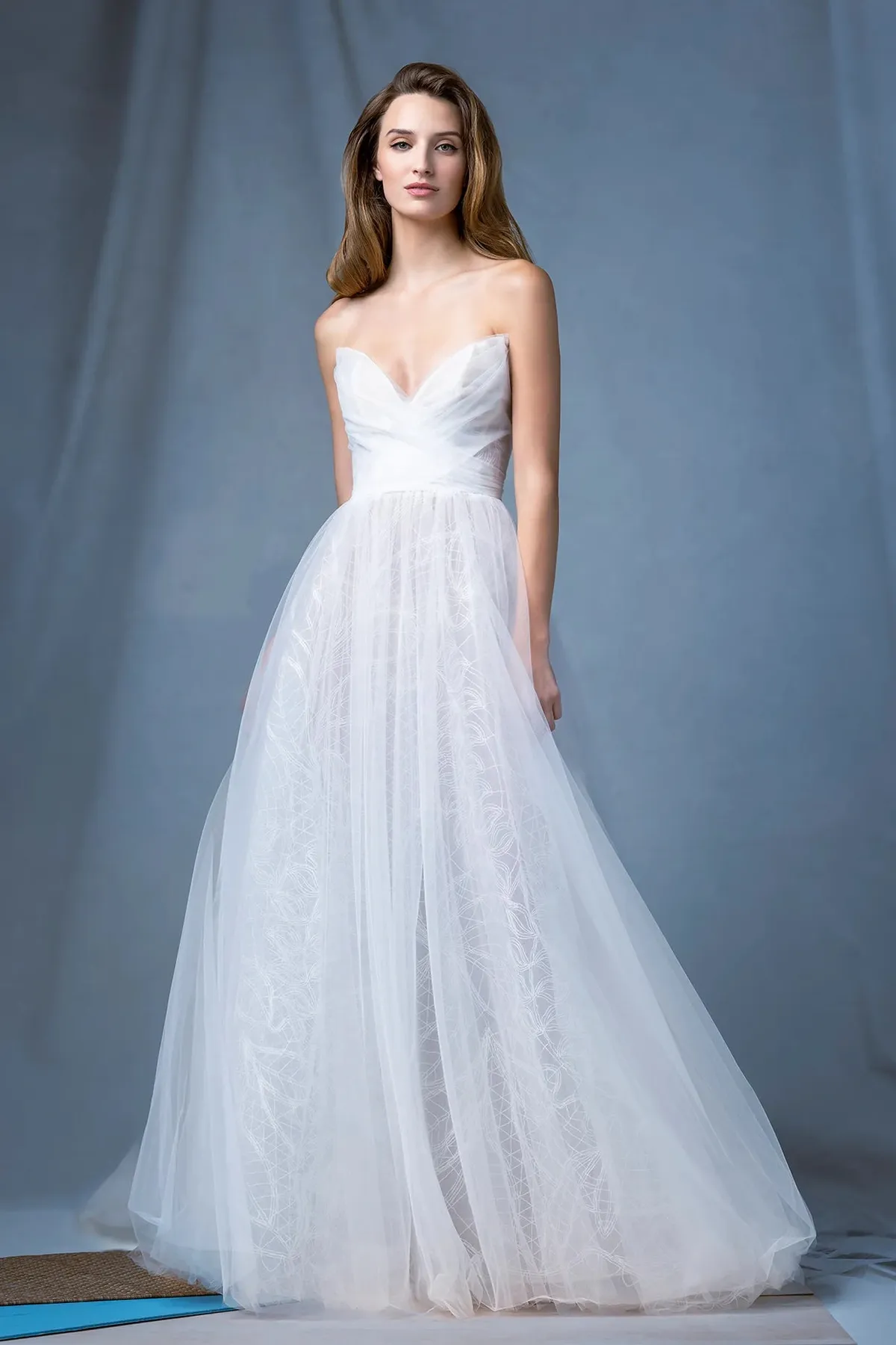 A model showcases the Ines Di Santo Grotto dress while standing in a photography studio with gray backdrop