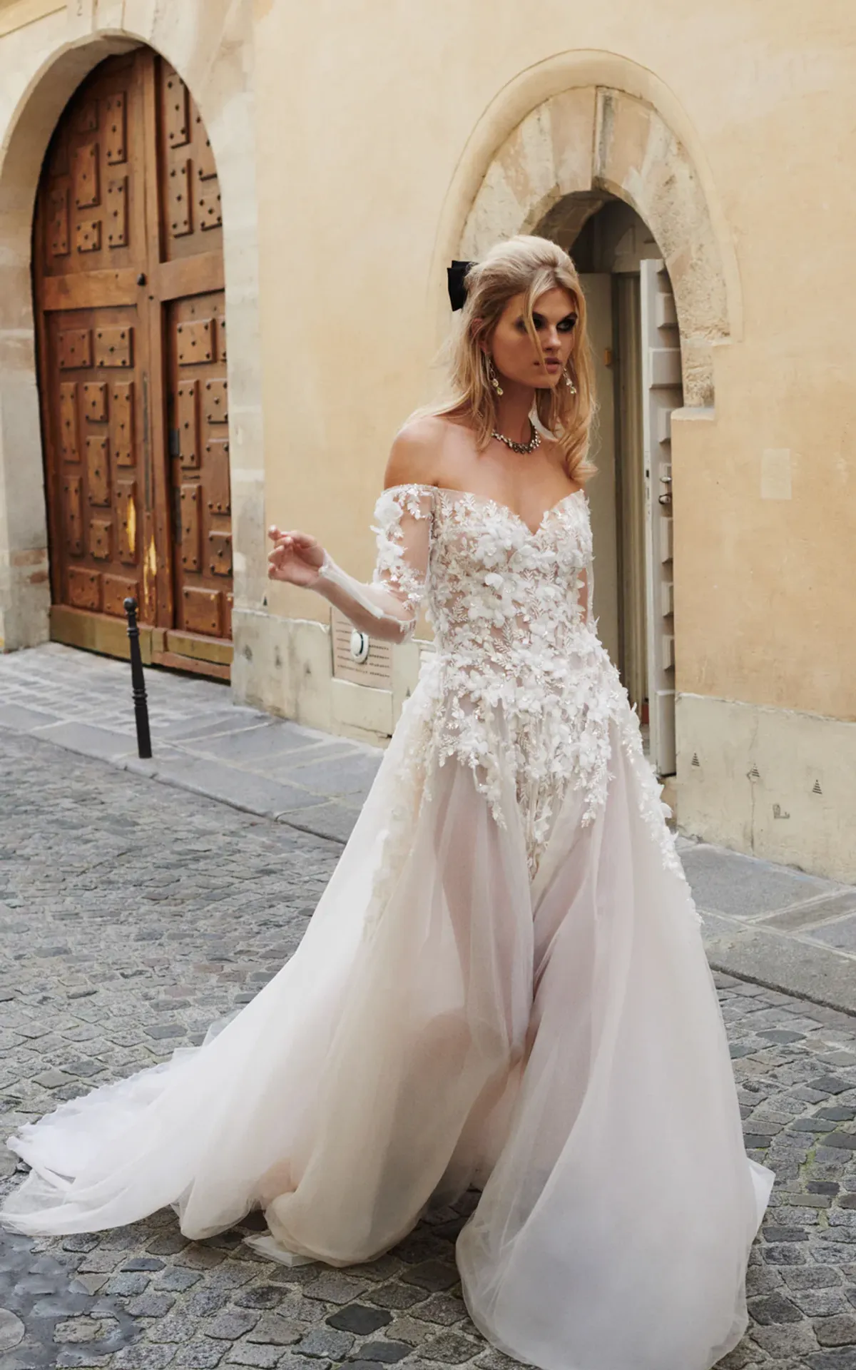 A model showcases the Galia Lahav Trish dress from the GALA collection while walking on a cobblestone road