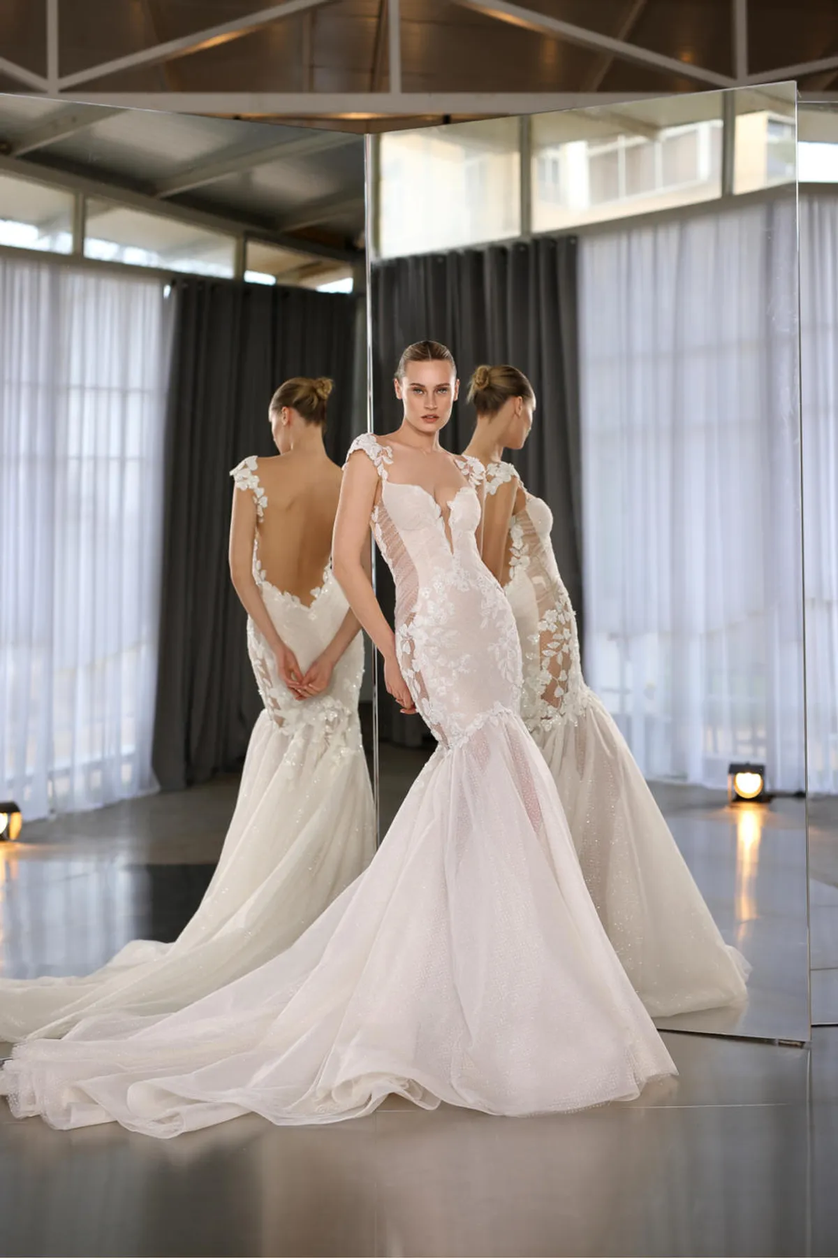A model showcases the Galia Lahav XO dress from the Couture collection in front of two angled mirros inside a studio