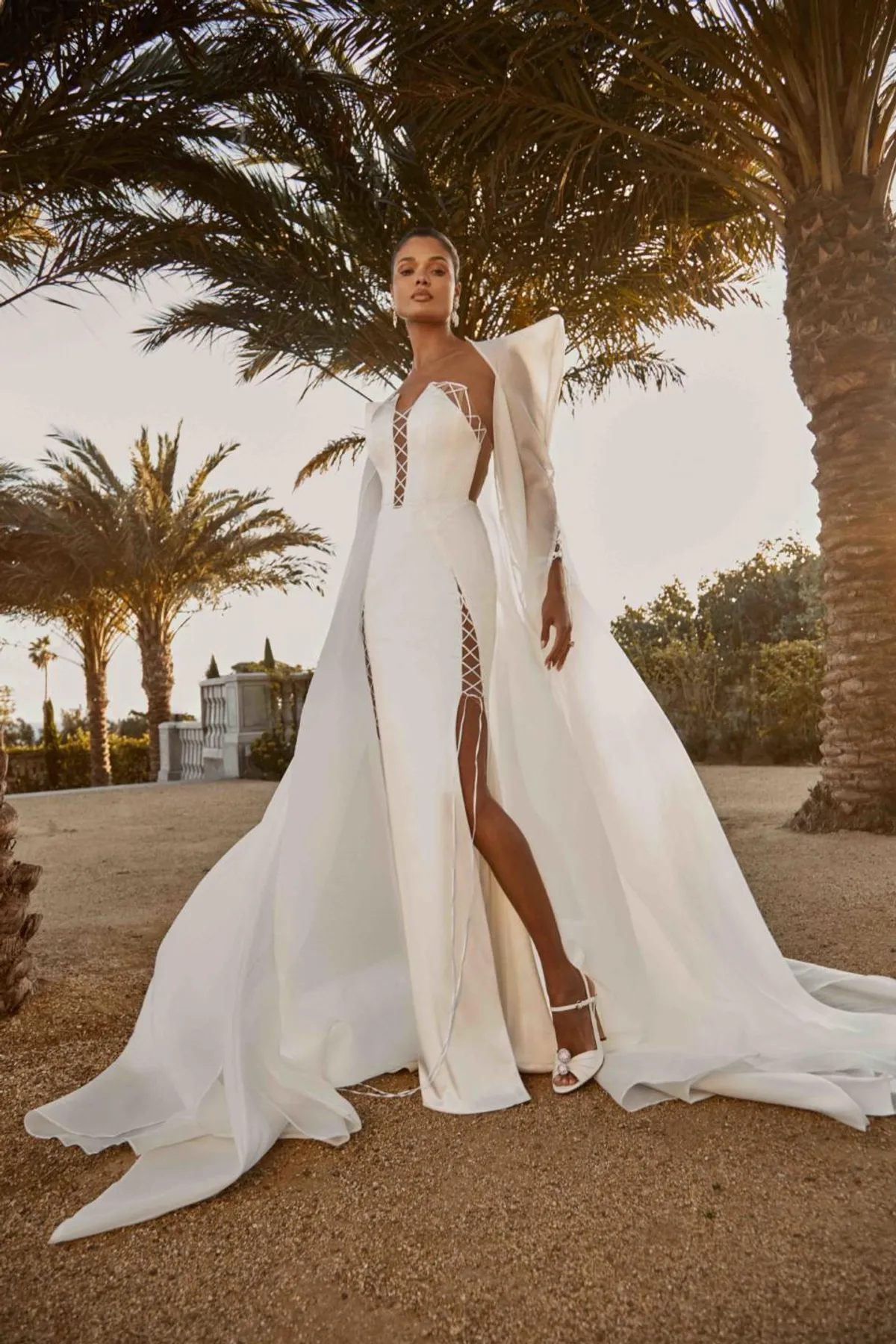 A model showcases the Galia Lahav Aspen dress from the Couture collection outside with palm trees in background