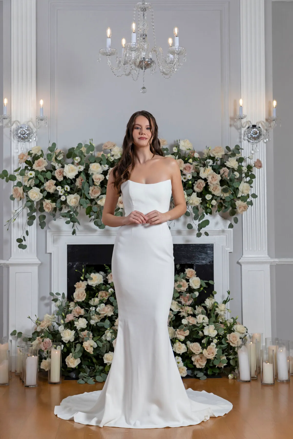 A model showcases the Angel Rivera Aster dress in front of a fireplace adorned with flowers and candles