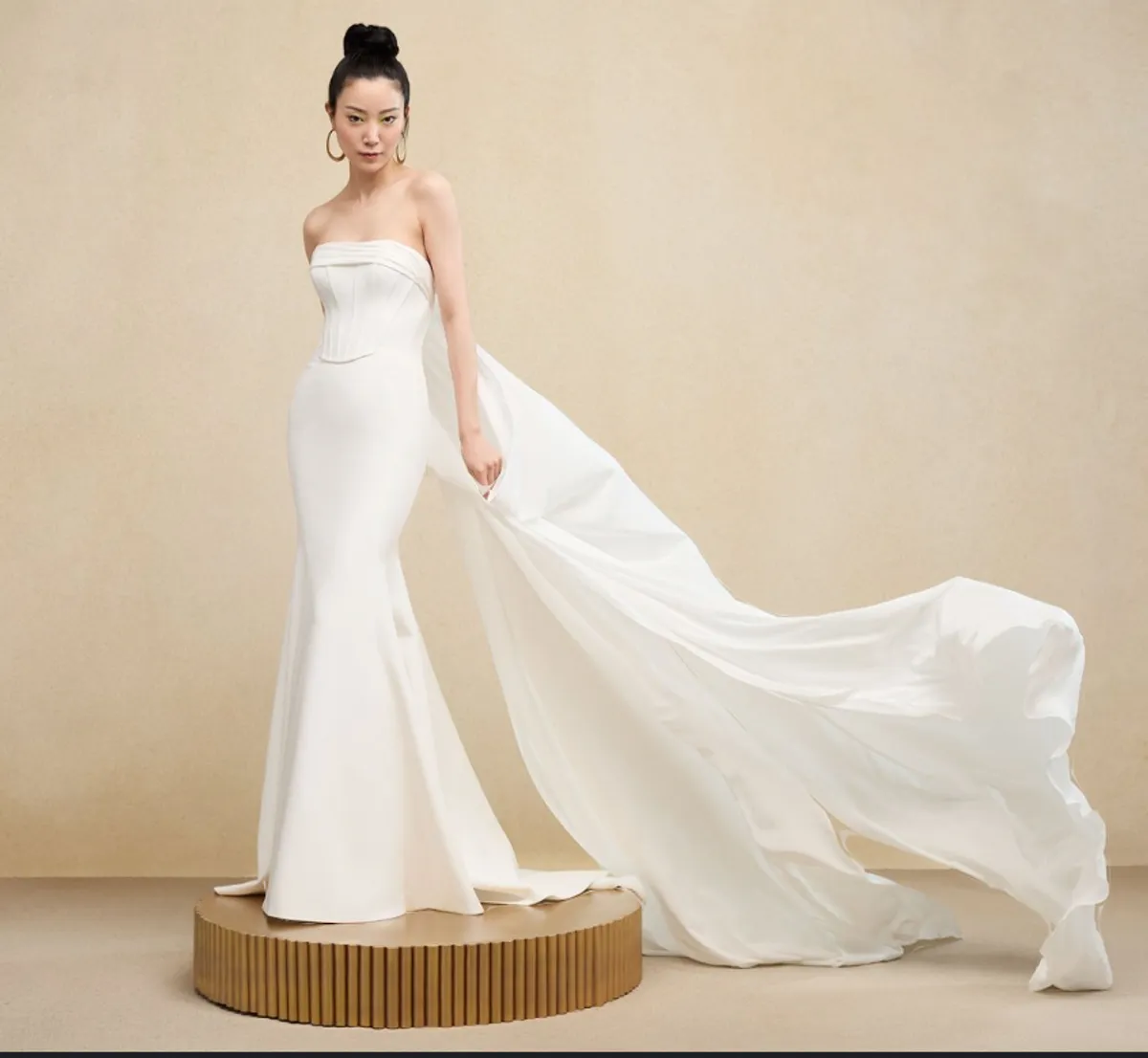 A model showcases the Ines Di Santo Brio dress while standing on a gold cirlce in a gold colored room