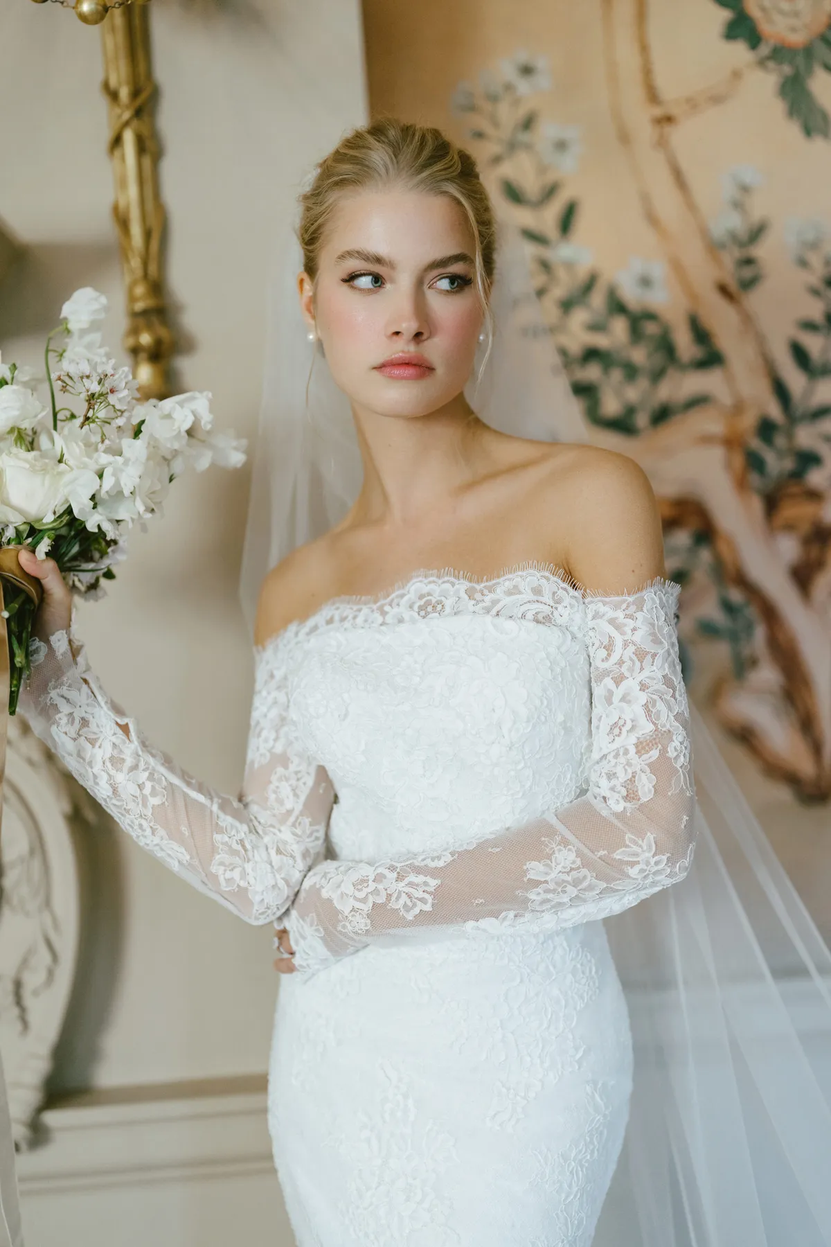 A model showcases the Anne Barge Collier dress from the Blue Willow Bride collection in a house with elegant white-painted woodwork and old french style wallpaper