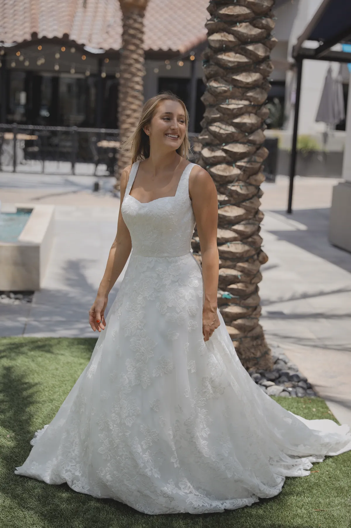 A model showcases the Angel Rivera Flora dress while standing near a palm tree