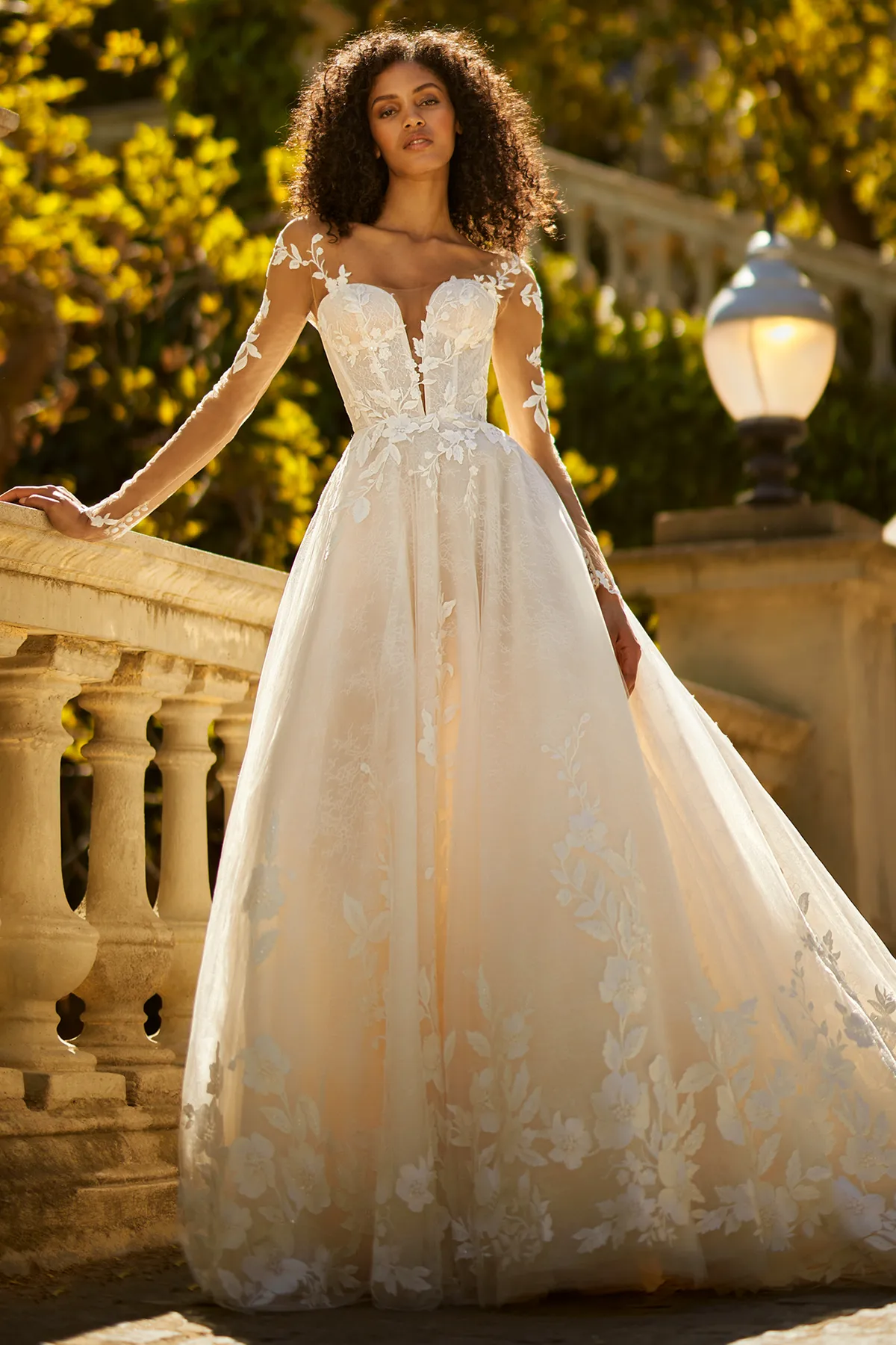 A model showcases the Ines Di Santo Forte dress from the Ines by Ines Di Santo collection on a stone bridge with greenery