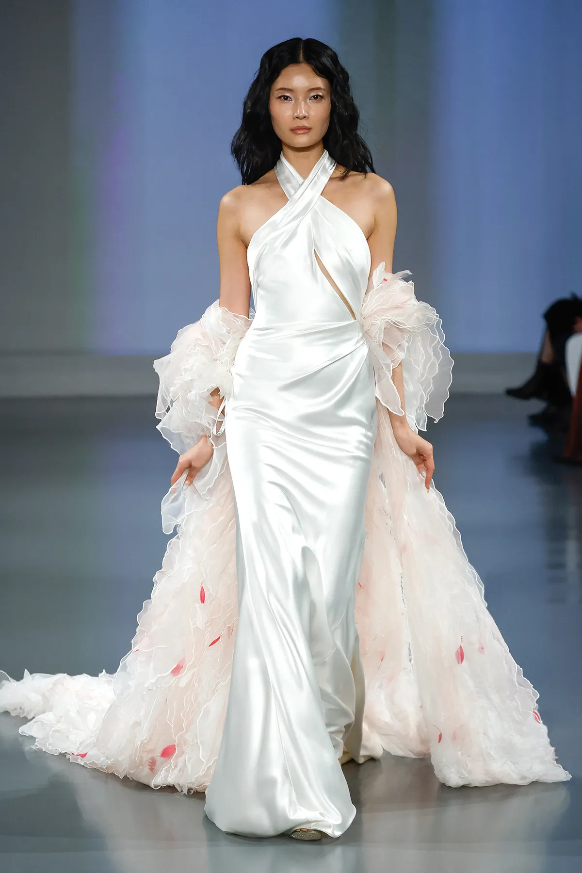 A model showcases the Ines Di Santo Ida dress while walking on a runway with a blue colored background
