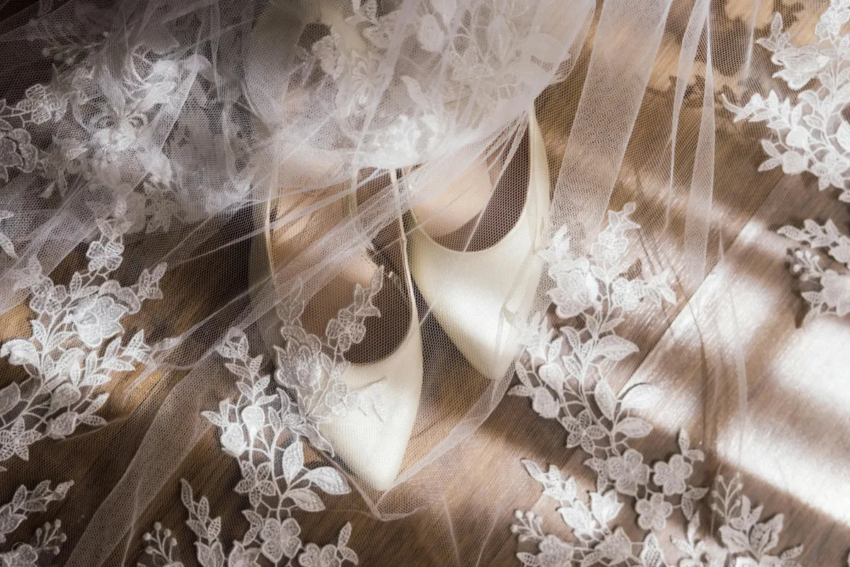 Lace with embroidered flowers covers a pair of white heels in a wedding detail image