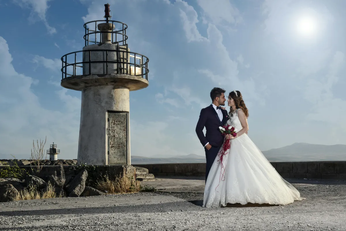 A bride and groom pose on a sunny day near a maritime on-shore beacon light as the gaze into each others eyes