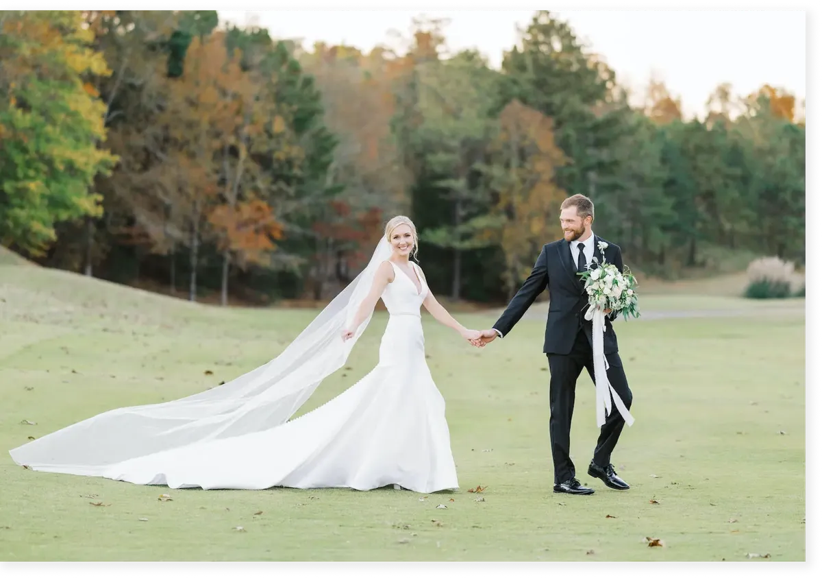 A groom and bride hold hands on a golf course while the bride is wearing an Antonio Gual dress and the groom holds her bouquet of flowers