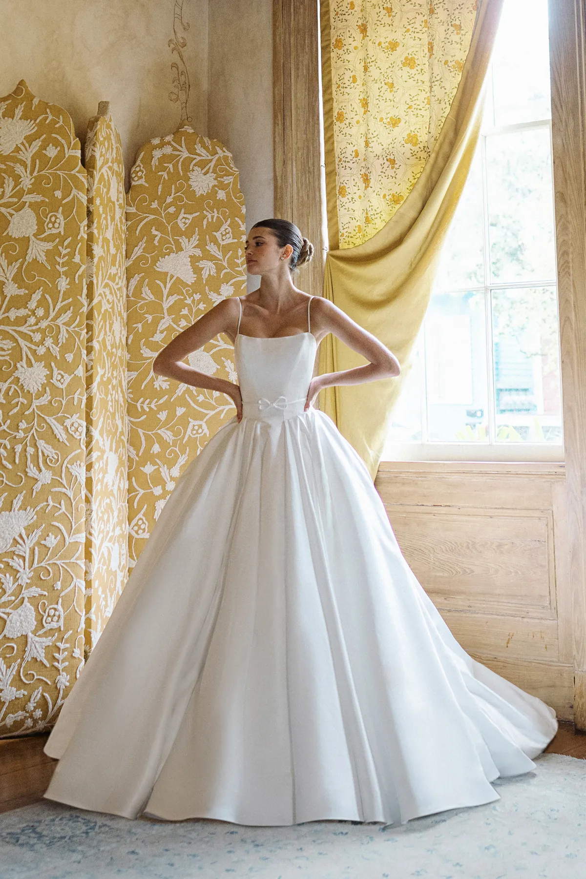 A model showcases the Anne Barge Monde dress in a room near a window with yellow and white accent furniture