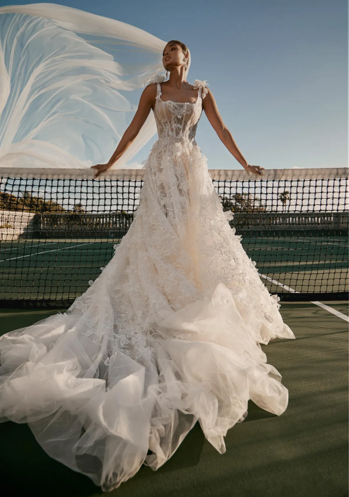 A model showcases the Galia Lahav Nirvana dress from the Couture collection on a tennis court while leaning on the net