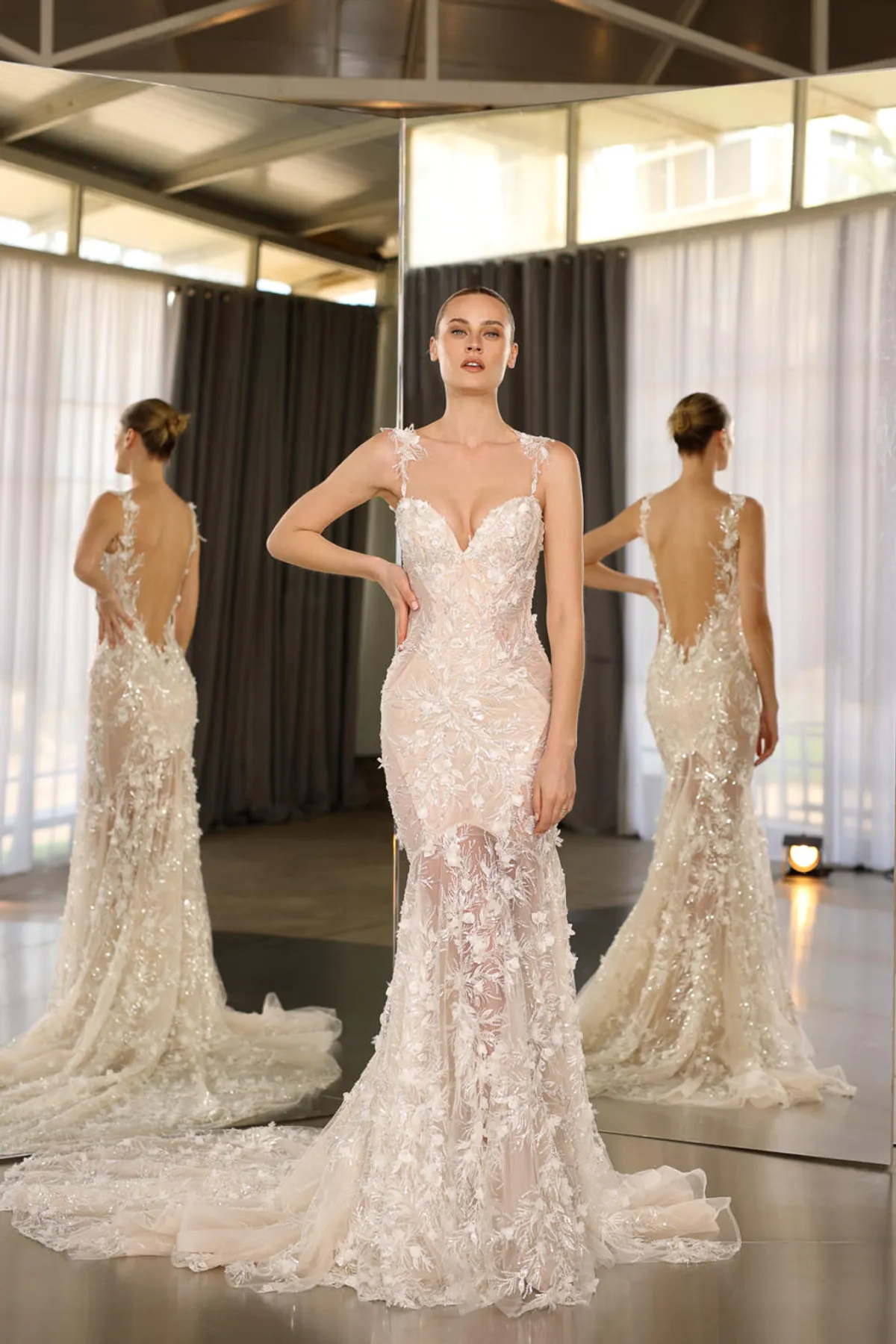 A model showcases the Galia Lahav Shiloh dress from the Couture collection in front of two angled mirros inside a studio